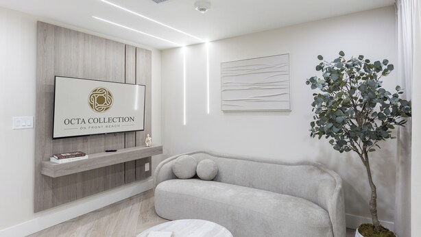 Una sala de estar moderna con un sofá gris, una mesa de centro blanca, un televisor montado y una planta en maceta.