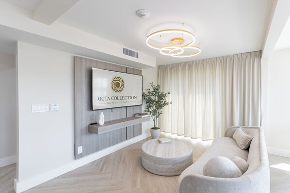 A modern living room with a mounted TV, a round coffee table, a sofa, and a potted plant. - Octa Collection on Front Beach (Panama City Beach)
