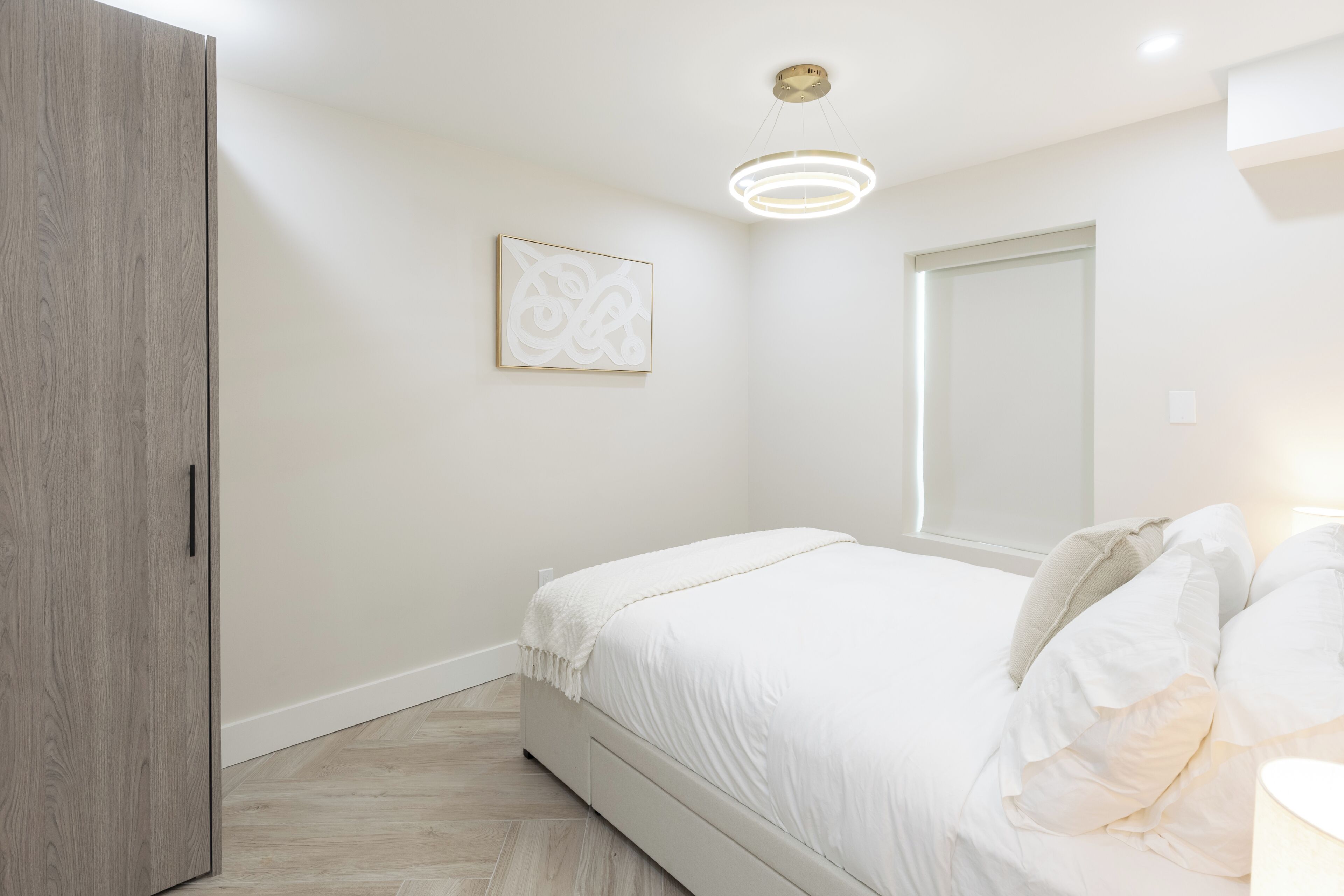 A bedroom with a bed, a wardrobe, a ceiling light, and a wall-mounted picture.