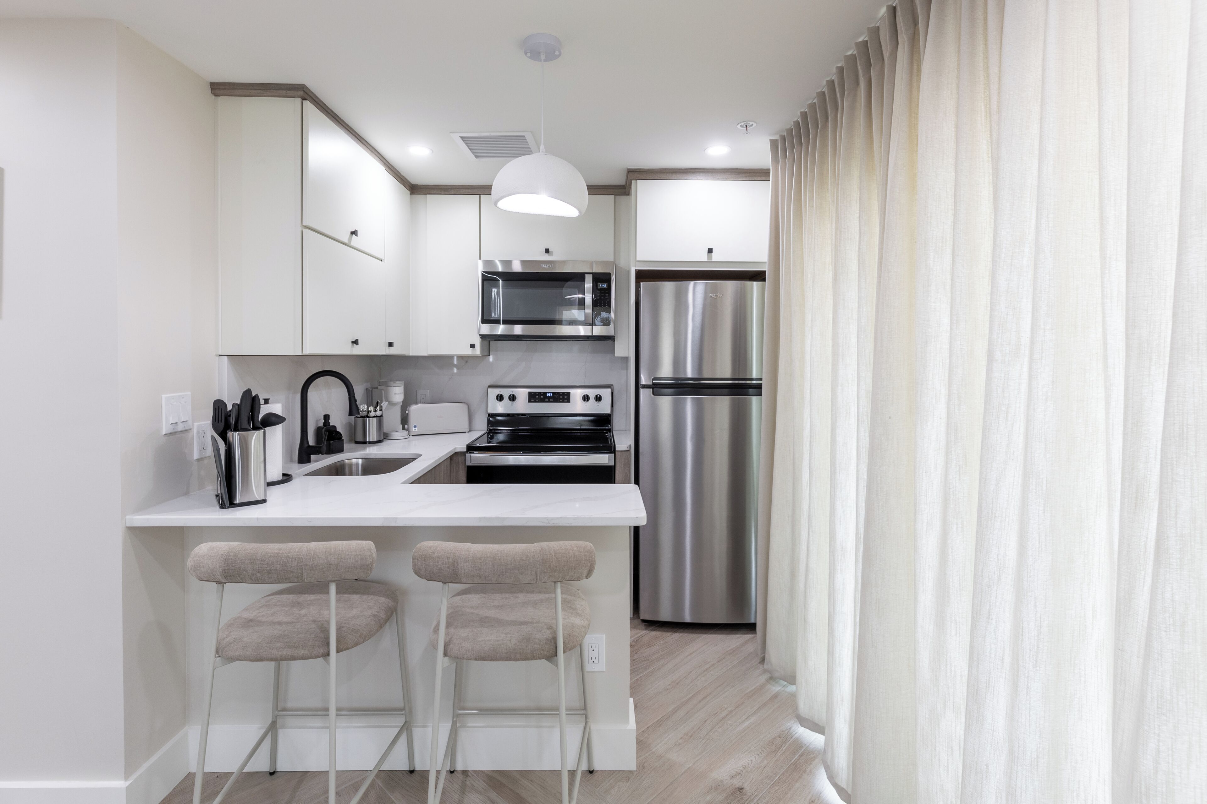 Una cocina moderna con armarios blancos, electrodomésticos de acero inoxidable y una zona de asientos con taburetes de bar.