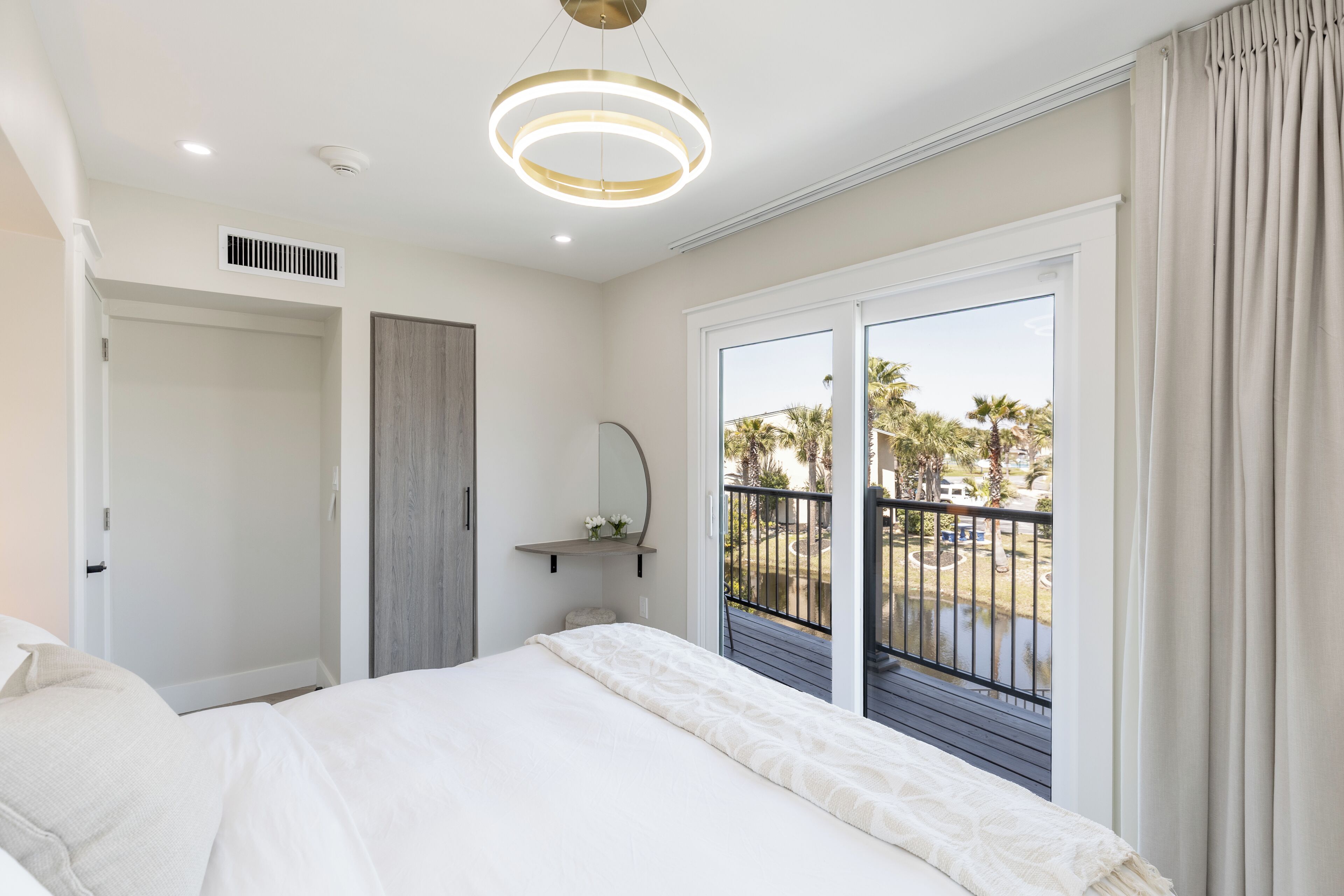 A bedroom with a bed, a bedside table, a mirror, and a view of the outdoors through a sliding door.