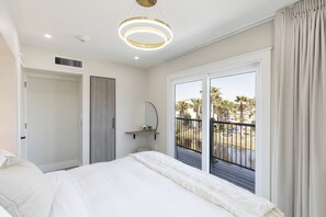 A bedroom with a bed, a bedside table, a mirror, and a view of the outdoors through a sliding door. - Octa Collection on Front Beach (Panama City Beach)