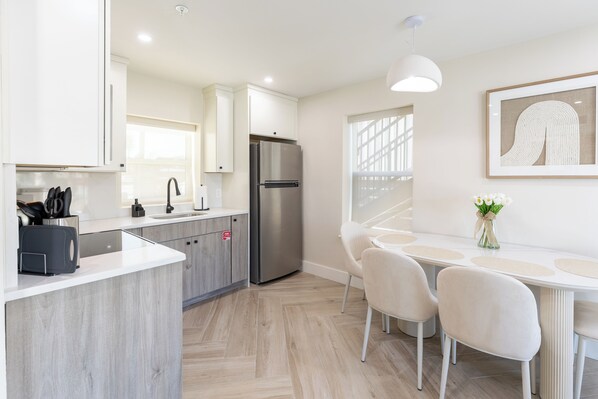 A modern kitchen with a built-in island, stainless steel appliances, and a dining area with a white table and chairs.