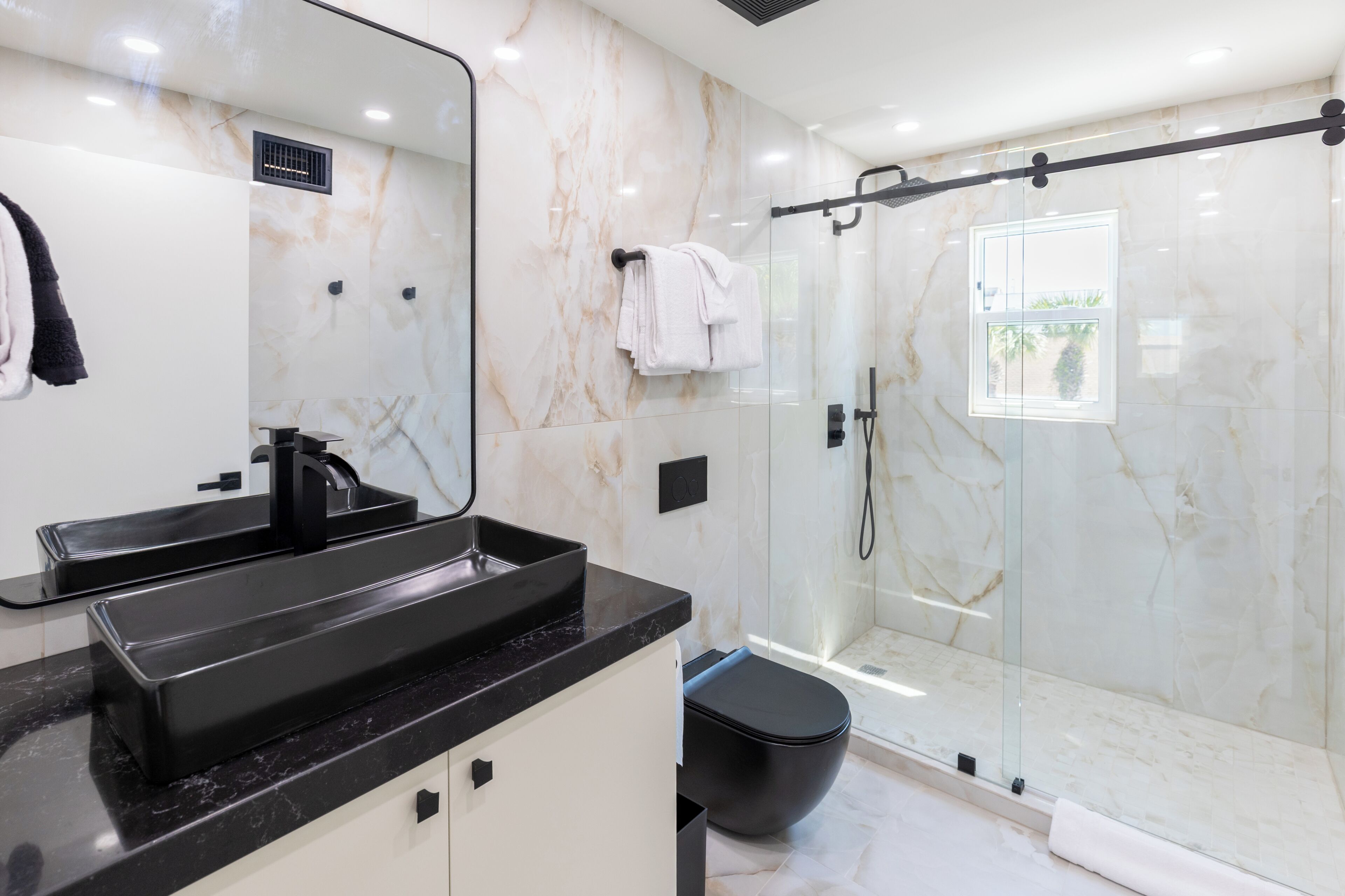 Ein modernes Badezimmer mit einem schwarzen Waschbecken, einer Duschkabine aus Glas und einer Marmorwand.
