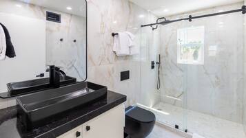 Ein modernes Badezimmer mit einem schwarzen Waschbecken, einer Duschkabine aus Glas und einer Marmorwand.