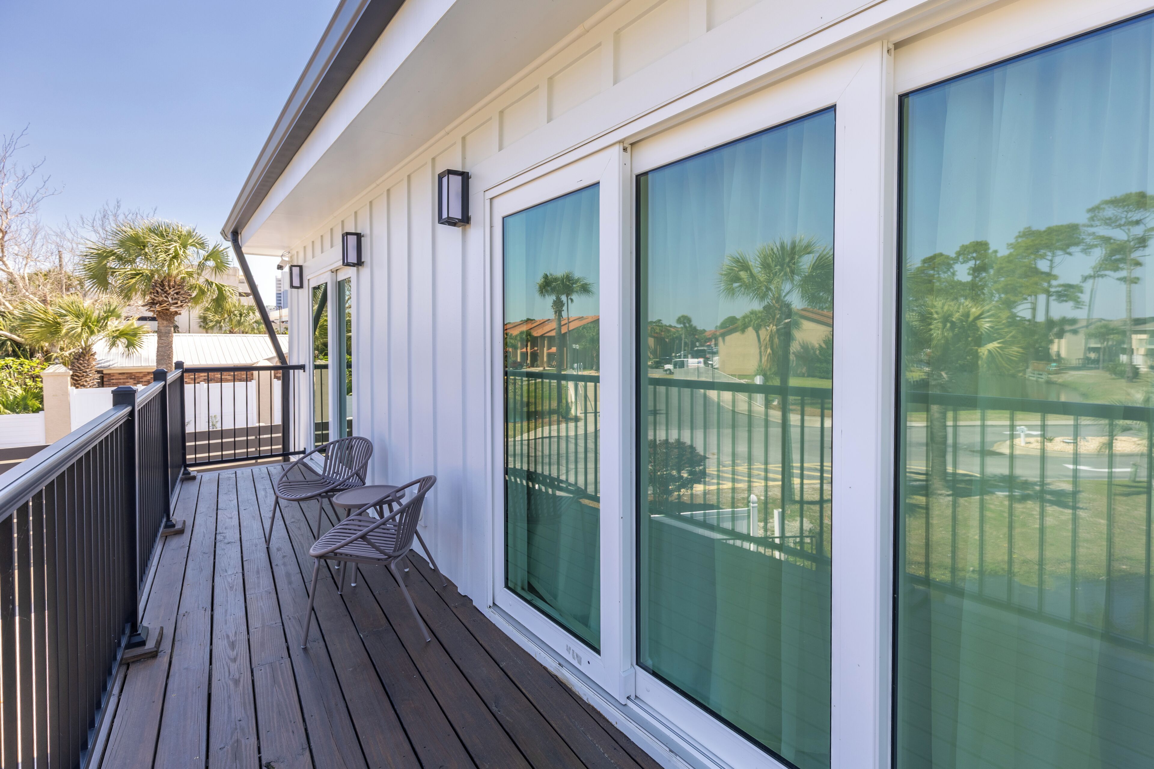 A wooden deck with outdoor furniture, large sliding glass doors, and a view of a residential area with palm trees.