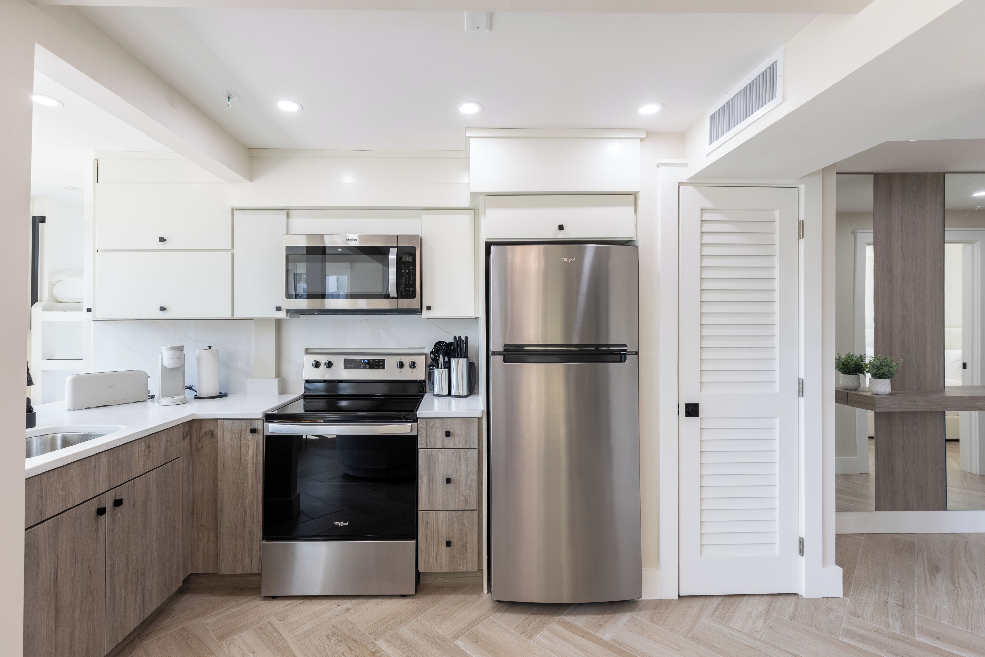 Une cuisine moderne dotée d’appareils électroménagers en acier inoxydable, de meubles en bois et d’un plancher à motifs en chevrons.