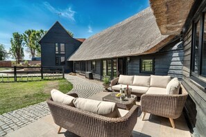 A modern house with a thatched roof, a patio with wicker furniture, and a view of a neighboring building. - Maggie Thaxted Barn Collection
Beautiful 4-bedroom Barn-ideal Countryside escape (Thaxted)