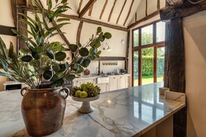 A kitchen with a marble countertop, a rustic vase with green plants, and a bowl of fruit. - Maggie Thaxted Barn Collection
Beautiful 4-bedroom Barn-ideal Countryside escape (Thaxted)