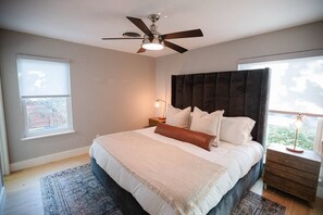 A bedroom with a bed, a ceiling fan, a nightstand, a lamp, and a window. - South Congress Oasis | Pool, Hot Tub & Sunroom (Austin)