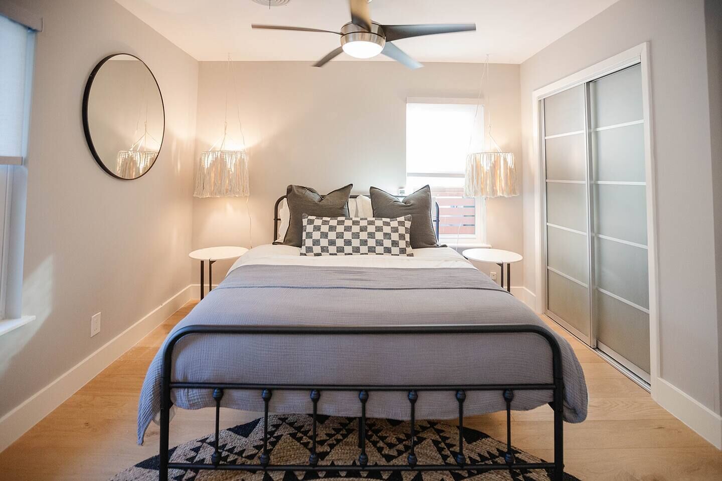 Une chambre à coucher comprenant un lit, des tables de chevet, un ventilateur de plafond, un grand miroir et une porte-fenêtre coulissante.