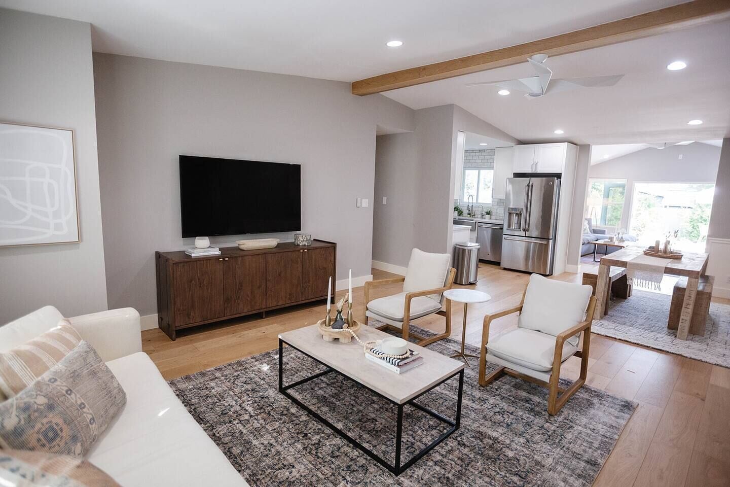A modern living room with a flat-screen TV, a wooden cabinet, and a dining area with a table and chairs.