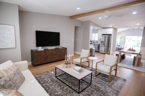 Una sala de estar moderna con televisor de pantalla plana, un mueble de madera y una zona de comedor con mesa y sillas.