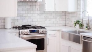 A modern kitchen with white cabinets, stainless steel appliances, and a patterned rug. - South Congress Oasis | Pool, Hot Tub & Sunroom (Austin)