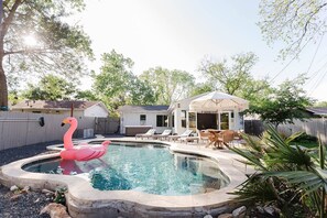 A backyard with a swimming pool, a flamingo float, lounge chairs, and a covered patio area. - South Congress Oasis | Pool, Hot Tub & Sunroom (Austin)