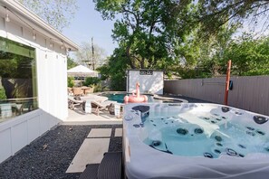 Ein Garten mit Whirlpool, einer Holzterrasse, Gartenmöbeln und einem kleinen Gartenhaus.