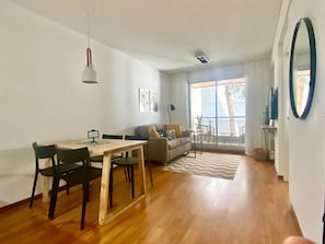 Ein modernes Wohnzimmer mit Essbereich, einer Couch, einem Couchtisch und einem großen Fenster mit Vorhängen.