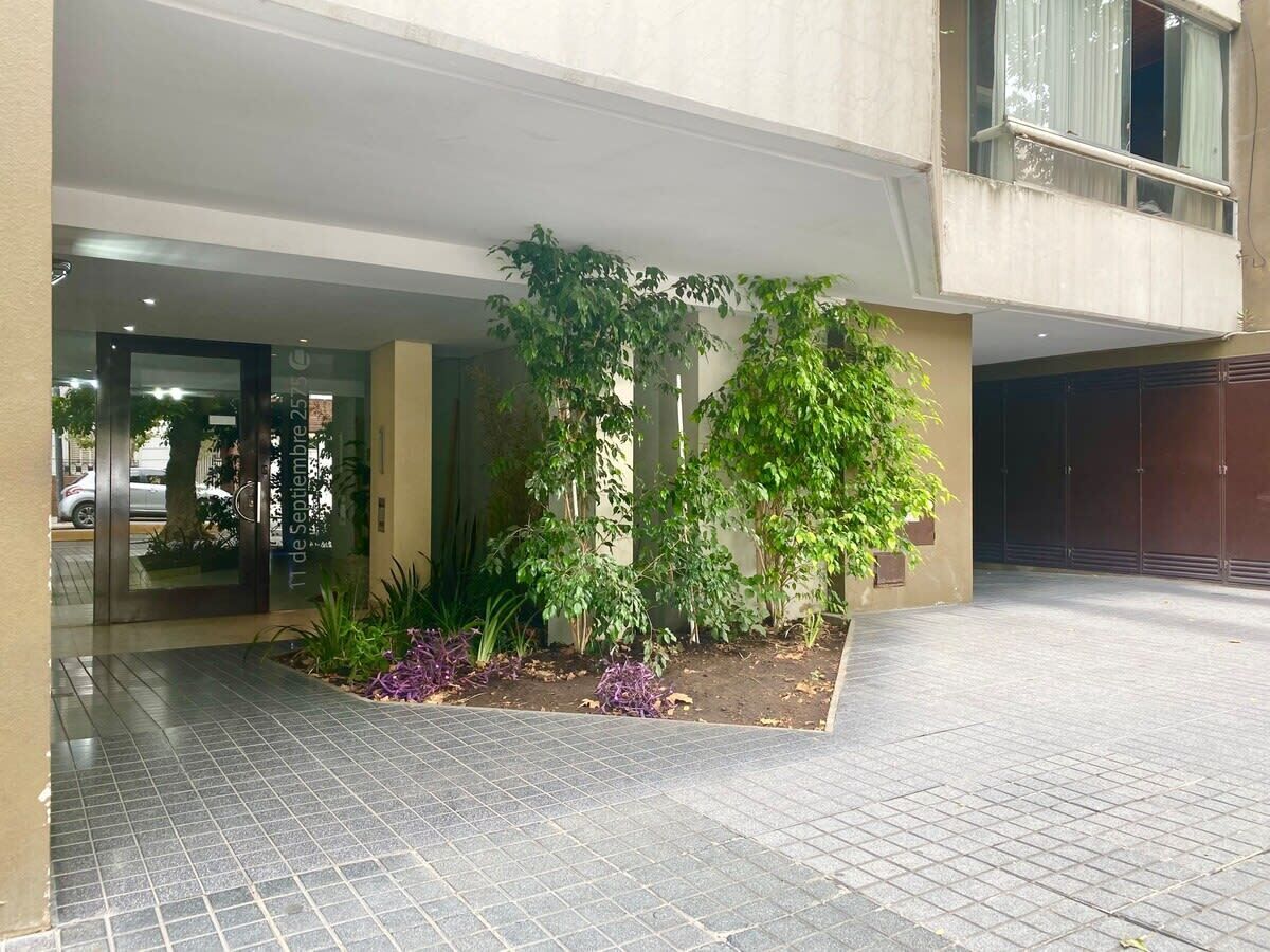 A building entrance with a paved area, a small garden with plants, and a glass door entrance.