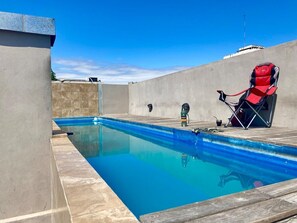 Ein Schwimmbecken mit Holzterrasse, einem roten Stuhl und einer Wasserflasche.