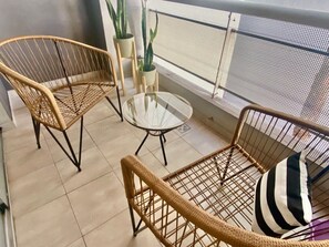 Ein Balkon mit Korbmöbeln, darunter zwei Stühle und ein Tisch, sowie mit Topfpflanzen.
