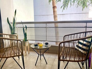 Ein Balkon mit zwei Korbstühlen, einem runden Tisch mit Glasplatte und einem Blumentopf.