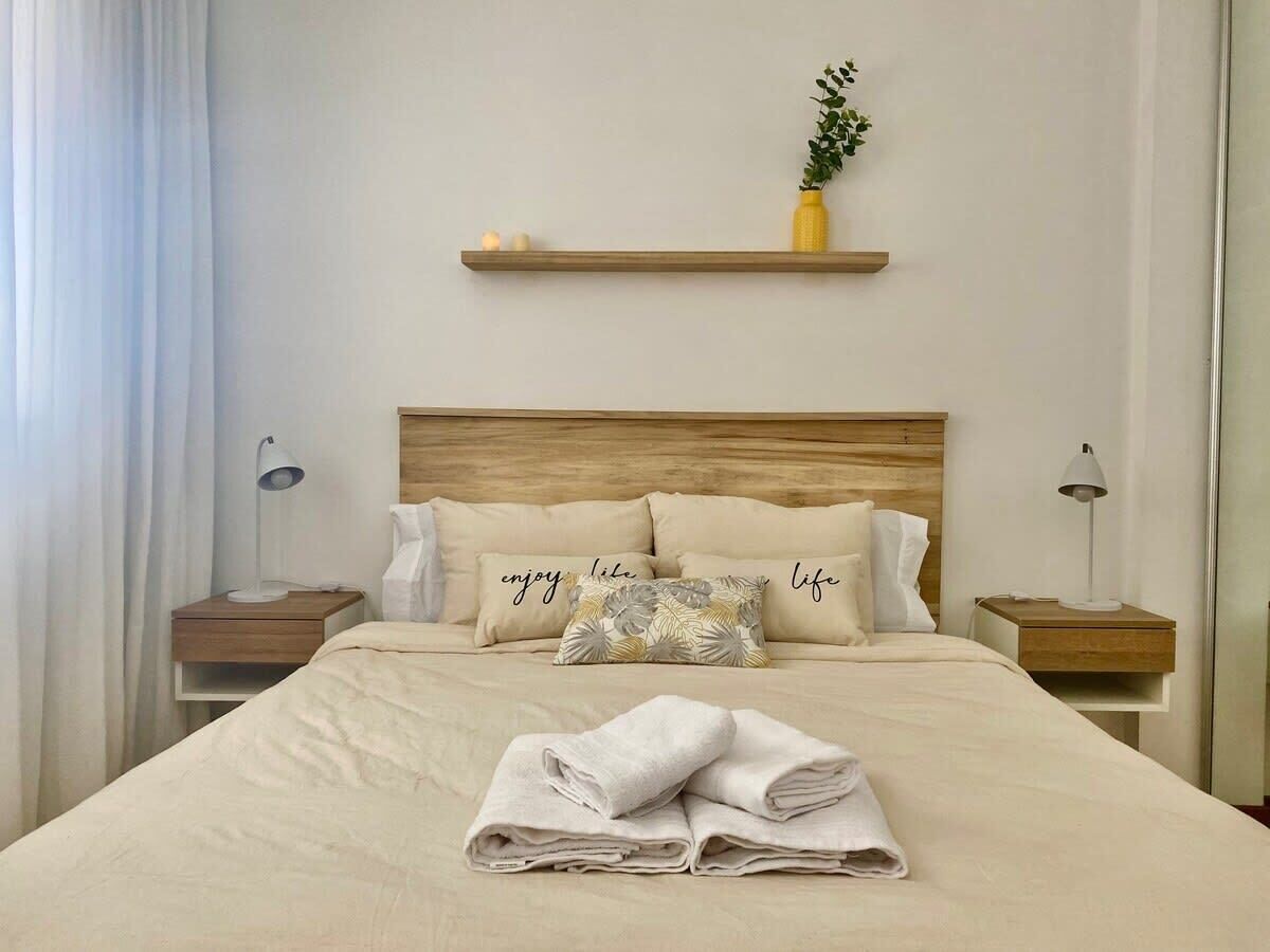 A neatly made bed with a pillow that says 'enjoy life' and a folded towel on the bed.