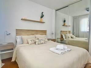 Une chambre d’hôtel avec un grand lit, des tables de chevet, un miroir et une étagère avec une plante.