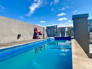 Une piscine sur le toit, avec un ciel bleu dégagé, une chaise rouge et un mur en béton.