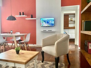 A modern living room with a beige armchair, a dining table with chairs, a TV mounted on the wall, and a bookshelf. - 157- Apt. with Great Location for 3 p. in Recoleta (Buenos Aires)