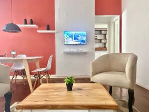 A modern interior with a wooden coffee table, a beige armchair, a television mounted on a white wall, and a dining area with chairs and a table. - 157- Apt. with Great Location for 3 p. in Recoleta (Buenos Aires)