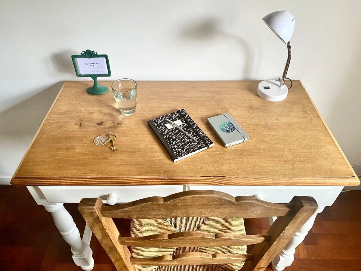 Une table en bois avec un pied blanc, un verre d’eau, un livre, une lampe et un petit panneau.