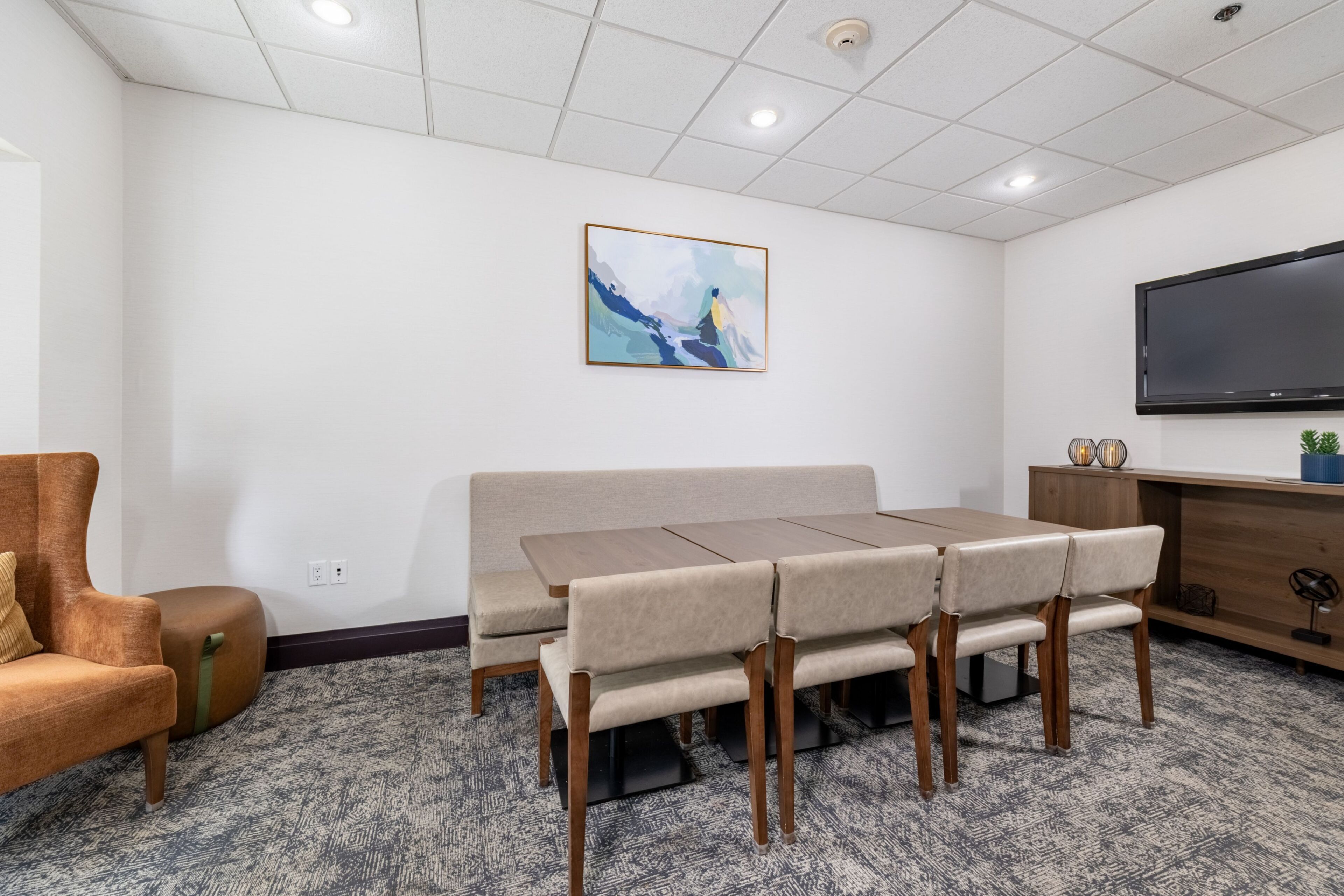 A conference room with a long table, chairs, a sofa, a TV, and a painting on the wall.