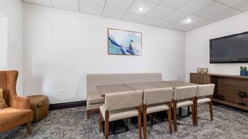 A conference room with a long table, chairs, a sofa, a TV, and a painting on the wall.