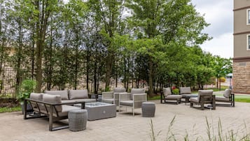 An outdoor patio area with seating arrangements, a fire pit, and surrounding trees.