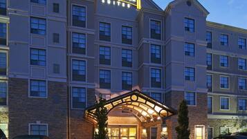 A multi-story hotel with a prominent Staybridge Suites sign, featuring a stone facade and a covered entrance with a curved roof.