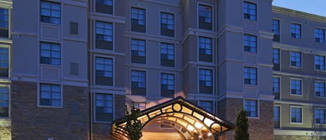 A multi-story hotel with a prominent Staybridge Suites sign, featuring a stone facade and a covered entrance with a curved roof.