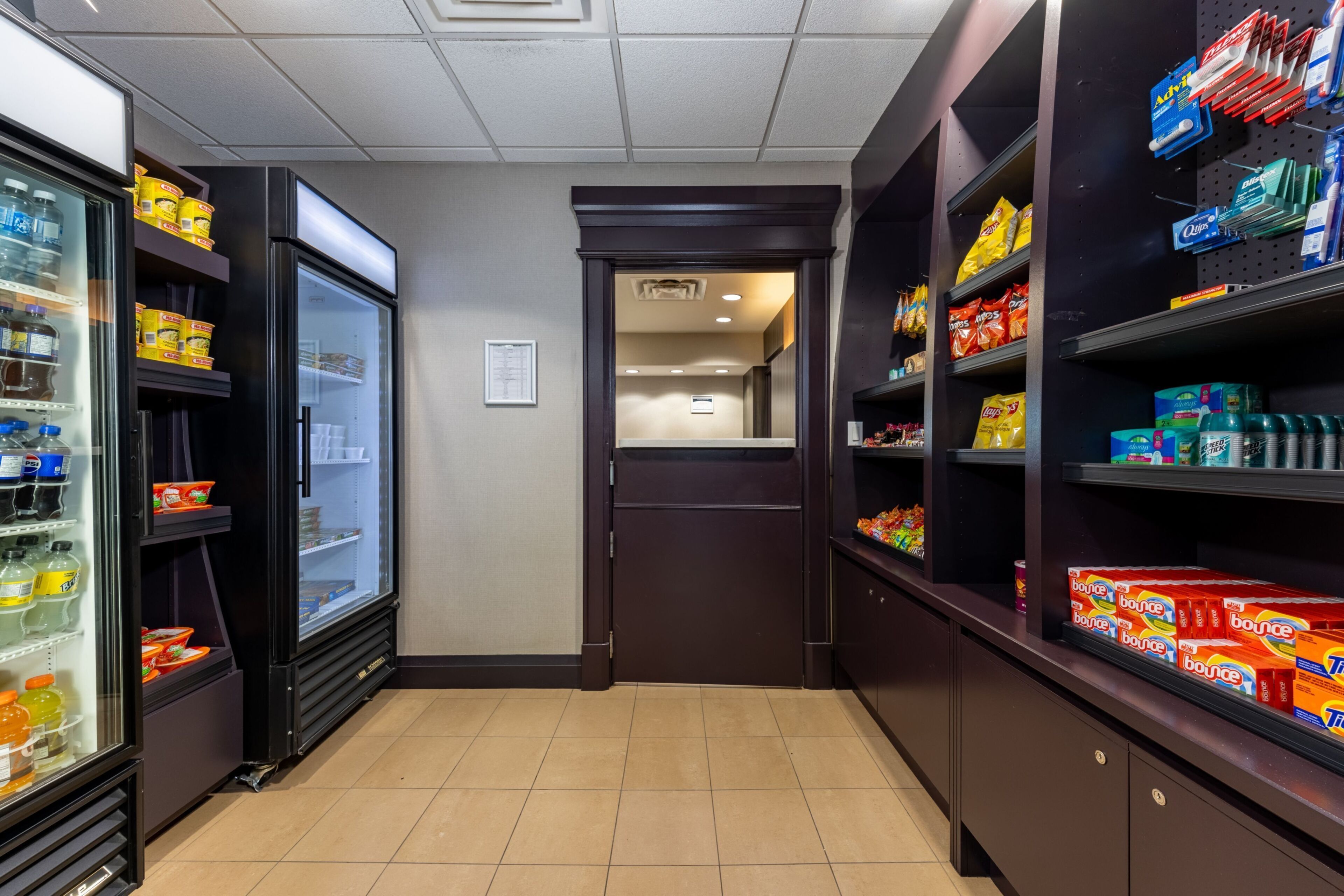 A corridor with shelves stocked with snacks and beverages, leading to a room with a door.