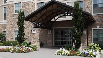 A hotel entrance with a stone facade, a covered entrance, and flower beds.