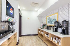 A modern kitchen area with a coffee station, a refrigerator with a Pepsi logo, and a framed artwork on the wall.