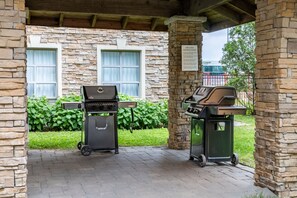 A patio area with two barbecue grills, a stone wall, and a sign with grilling instructions.