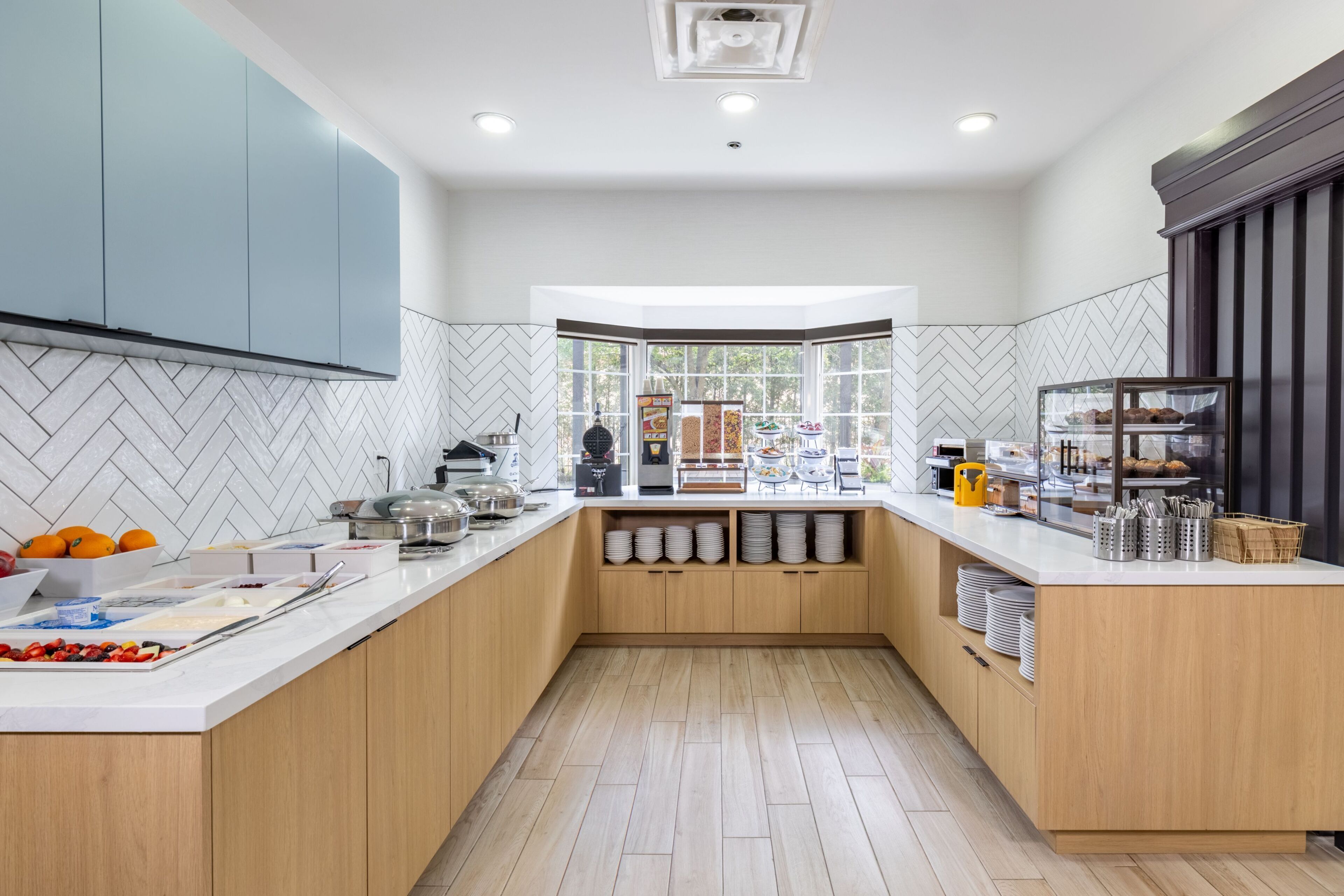 A modern kitchen with a central island, white countertops, and a herringbone tile backsplash.
