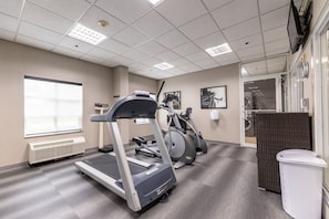 A fitness room with treadmills, elliptical machines, and a wall-mounted television.