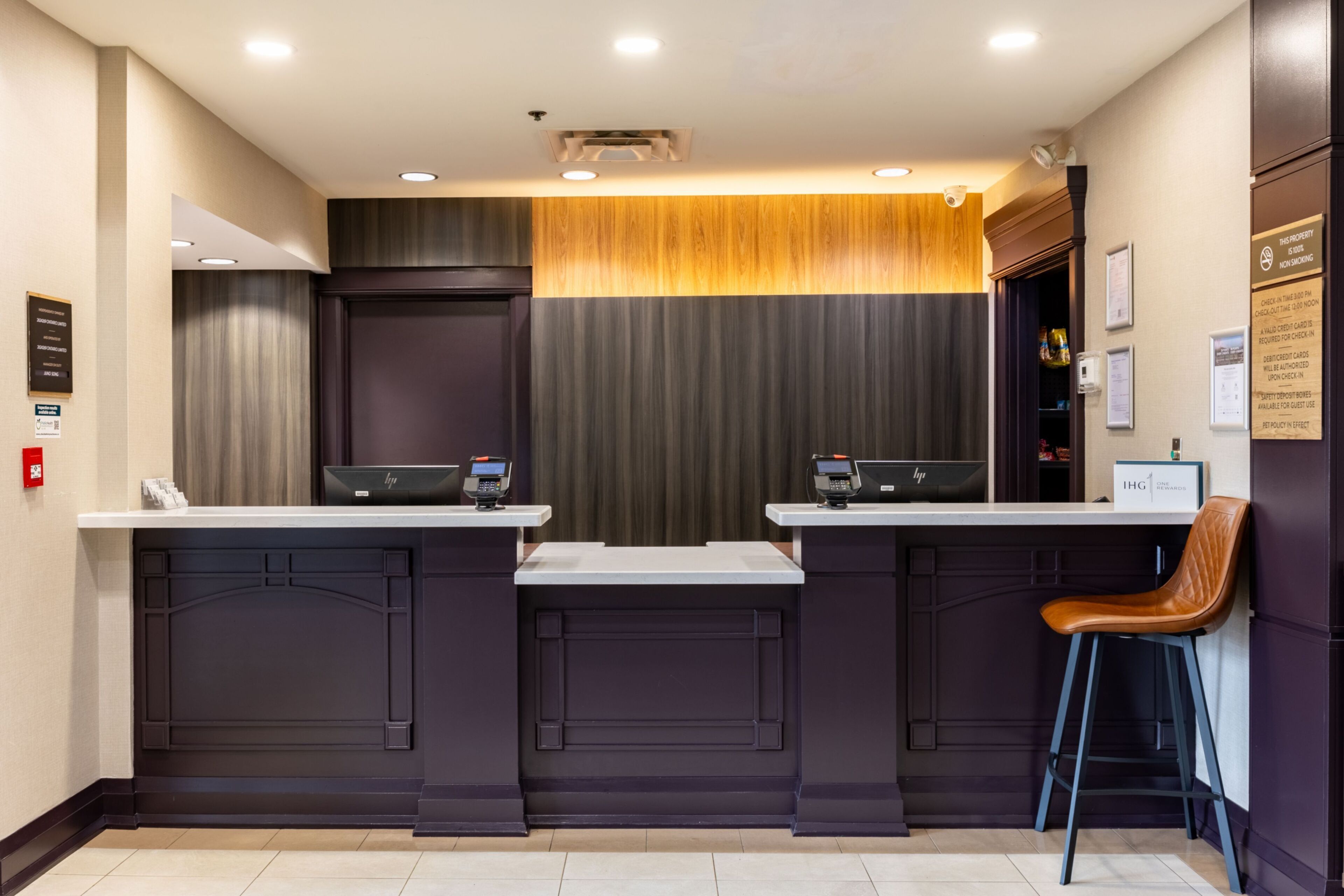 A modern hotel lobby with a reception desk, check-in counters, and a seating area.