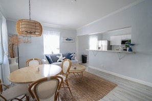 A modern living room with a dining area, featuring a round table, wicker chairs, and a hanging light fixture. - Renovated Coastal Hideaway • 2BR • Minutes to Beach • Private Parking & 65” TV (Boynton Beach)