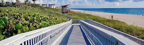 A boardwalk leading to a beach with a lifeguard tower, vegetation, and a clear sky.