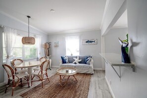 Ein Zimmer mit Esstisch, Stühlen, einer Couch mit Sternen-Kissen, einer Hängeleuchte und einem an der Wand befestigten Regal.