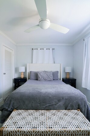 A bedroom with a bed, two bedside tables with lamps, a ceiling fan, and a window with curtains. - Renovated Coastal Hideaway • 2BR • Minutes to Beach • Private Parking & 65” TV (Boynton Beach)