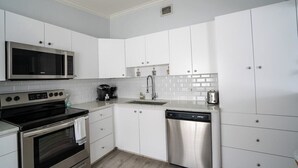 A modern kitchen with white cabinets, stainless steel appliances, and a tiled backsplash. - Renovated Coastal Hideaway • 2BR • Minutes to Beach • Private Parking & 65” TV (Boynton Beach)