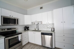 A modern kitchen with white cabinets, stainless steel appliances, and a tiled backsplash. - Renovated Coastal Hideaway • 2BR • Minutes to Beach • Private Parking & 65” TV (Boynton Beach)