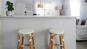 A kitchen with two bar stools, a window with sheer curtains, and a hanging light fixture. - Renovated Coastal Hideaway • 2BR • Minutes to Beach • Private Parking & 65” TV (Boynton Beach)